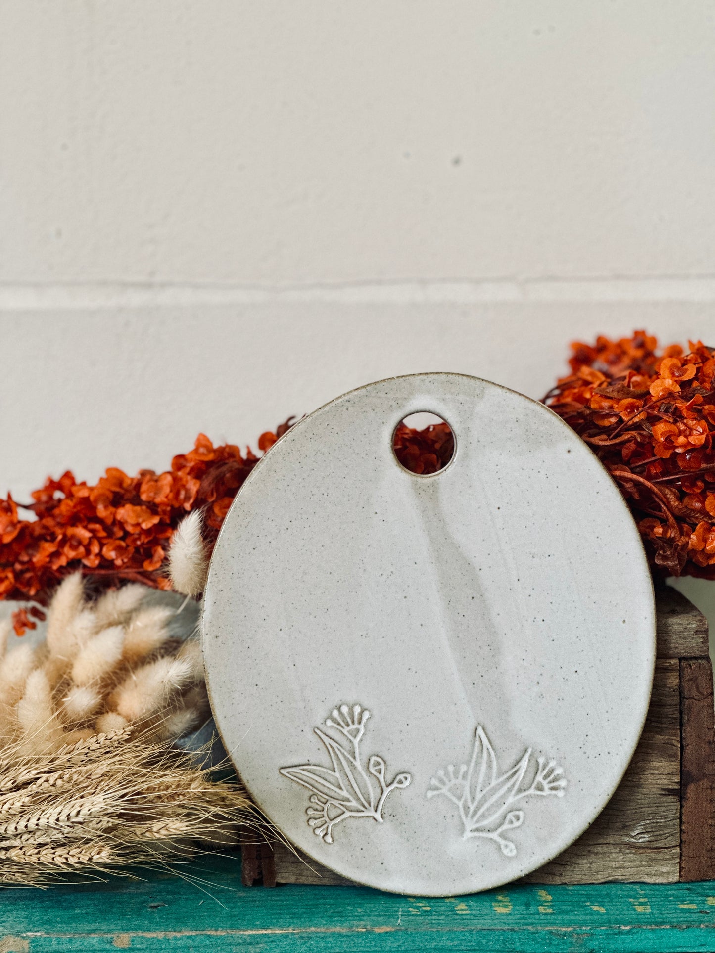 An oval shaped handmade ceramic cheese platter with gum leaves and flowers imprinted into the clay.