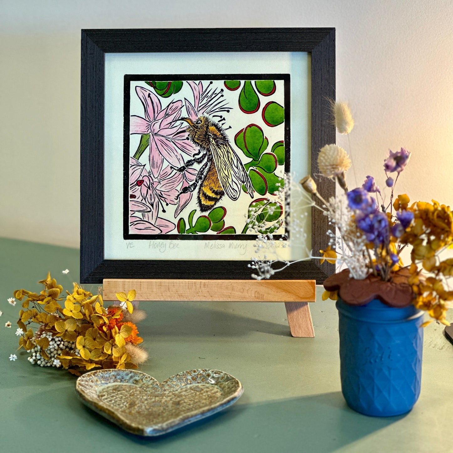 Honey bee artwork framed and sitting on sideboard with a vase of flowers