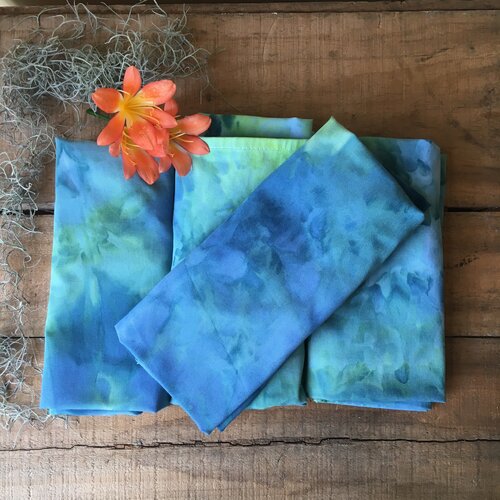 a pile of folded ice dyed child aprons in blues and greens