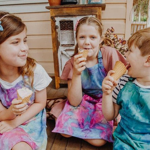 The children sitting and eating icecreams while wearing ice dyed aprons