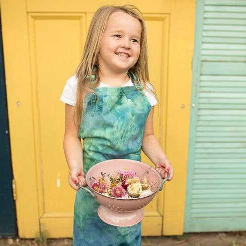 Little girl in an ice dyed childs apron collecting flowers in a bowl