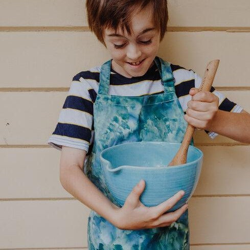 Young boy wearing an ice dyed apron while cooking.