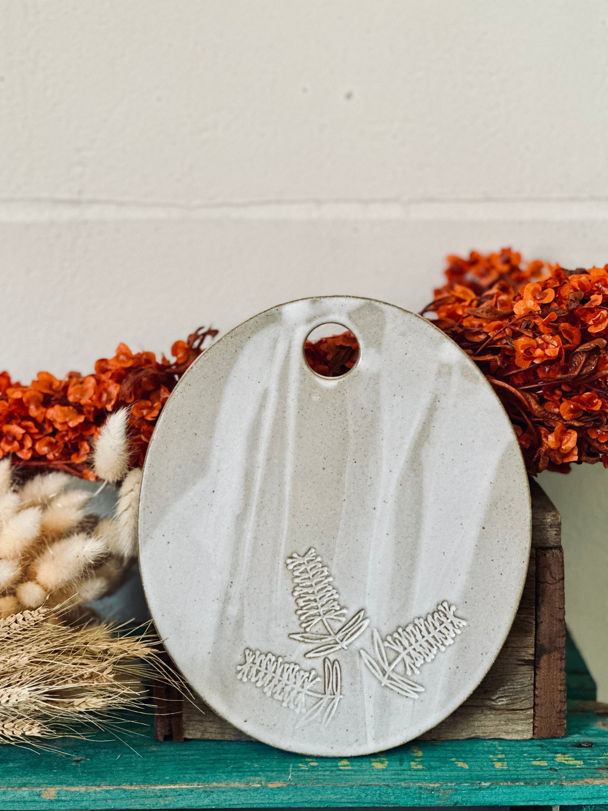 An oval shaped handmade ceramic cheese platter with bottle brush flowers imprinted into the clay.