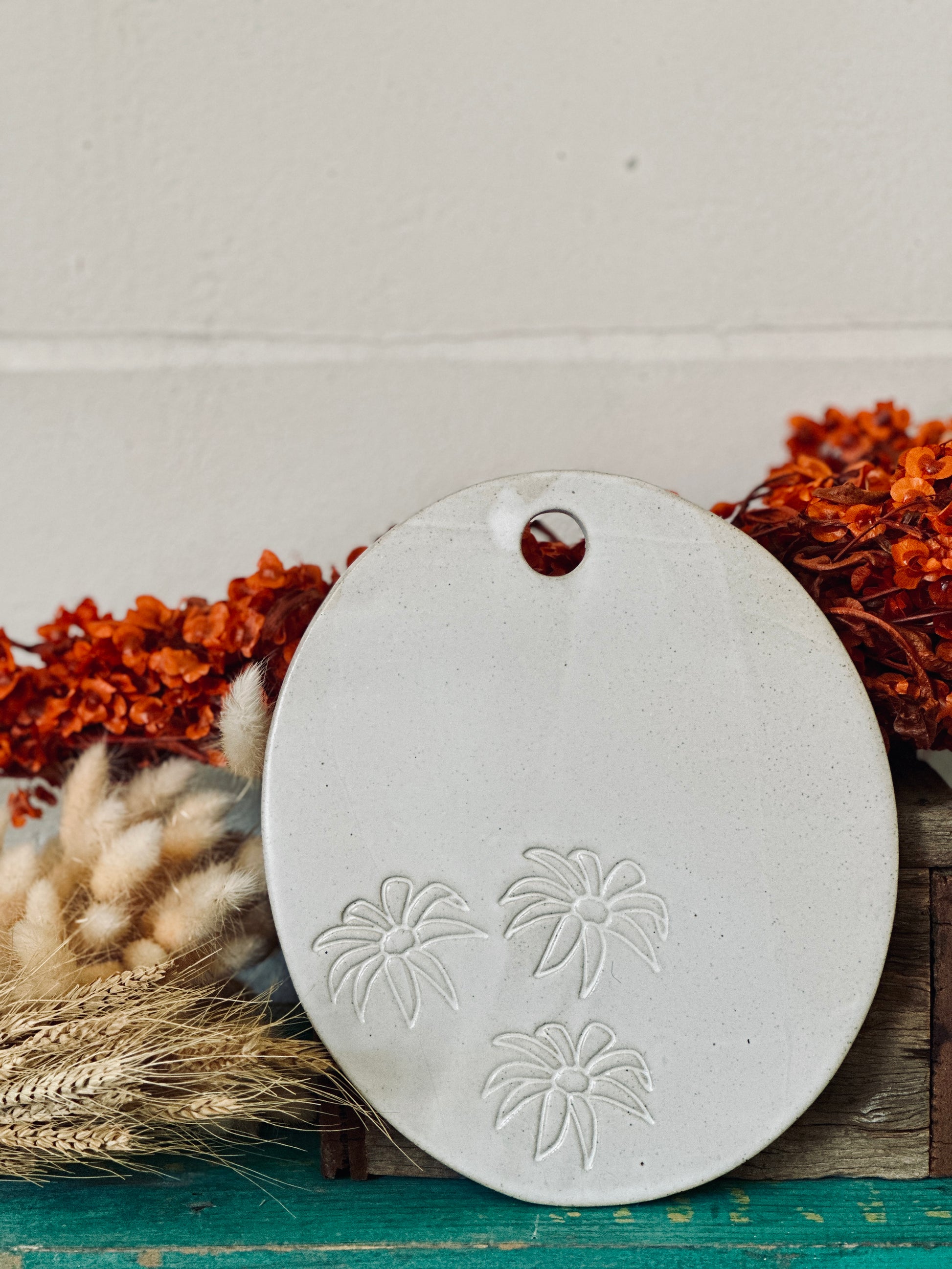 An oval shaped handmade ceramic cheese platter with flannel flowers imprinted into the clay.